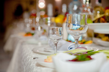 Festive tableware with glasses on a table. Empty glasses stand near plates and forks on banquet table decorated with white tablewear. Festively served table against blurred background in restaurant.