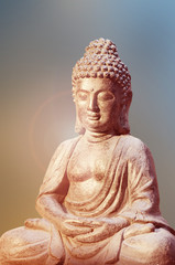 Buddha statue sitting in meditation pose against blurred golden background.