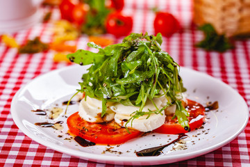 Caprese salad with arugula on white plate. Close up