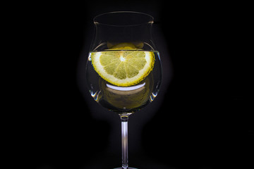 Glass of water with a slice of lemon with bubbles, isolated on a black background.