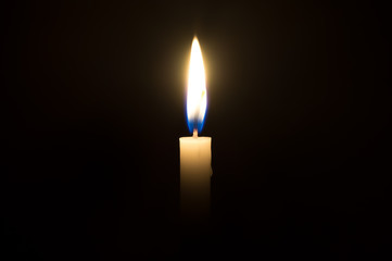 A single candle light glowing on a white candle in the middle part of frame on black background