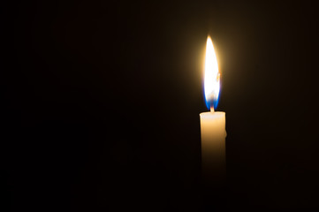 A single candle light glowing on a white candle on black background