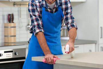 Man cleaning table with rag in kitchen, closeup