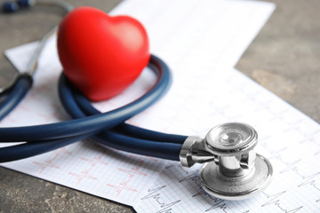 Stethoscope, red heart and cardiogram on gray table. Cardiology concept