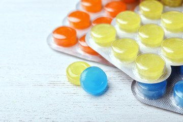 Blisters with color cough drops on white wooden background