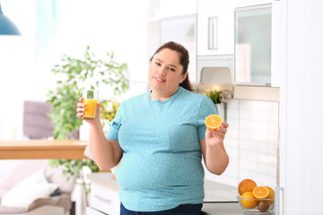 Overweight woman with glass of fresh juice and orange in kitchen. Healthy diet