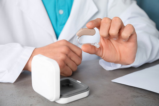 Doctor holding hearing aid at table, closeup. Medical device