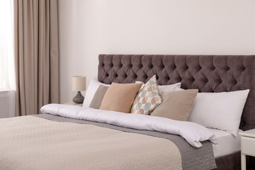 Large comfortable bed near light wall in simple room interior