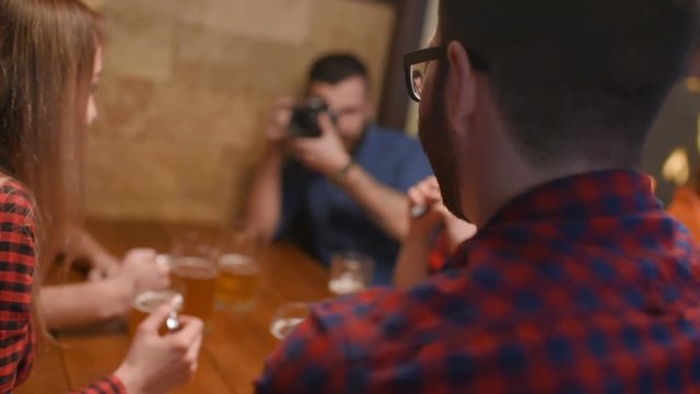 a group of friends - young guys and girls drinking beer, talking and smiling at the bar