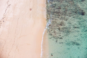 Vertical view of Pandawa Beach , Bali where 2 beachgoers are strolling next to each other as a wave comes in in front of them 