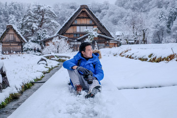 Fototapeta na wymiar Asian man smiling face during snowing at Shirakawa-go village in winter including traditional House Gassho style and one of UNESCO world heritage sites, Gifu, Japan