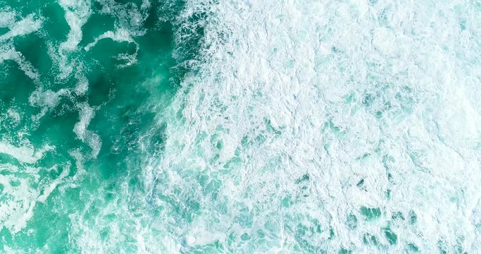 Slow motion top down aerial view of giant ocean waves crashing on sunny day 