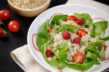 Quinoa salad with vegetables, raspberry and tomatoes on the black table. Super food for healthy and concept of balanced diet
