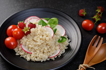 Quinoa salad with vegetables, raspberry and tomatoes on the black table. Super food for healthy and concept of balanced diet