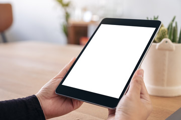 Mockup image of hands holding black tablet pc with blank white screen while sitting in office