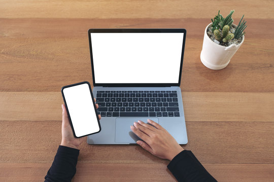 Top View Mockup Image Of A Hands Holding A Blank White Screen Mobile Phone And Laptop On Wooden Table In Office