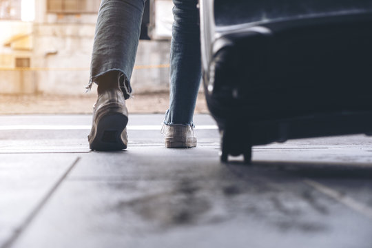 Closeup image of a woman's feet while traveling and dragging a black baggage in the outdoors