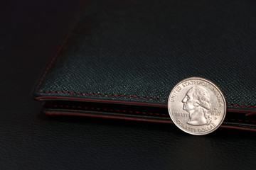 A quarter of US Dollar coins on obverse (USD) with black wallet on black floor.