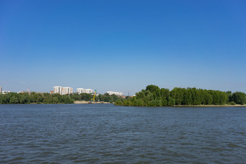 urban landscape with views of the Ob river and coastline with houses against a blue sky.
