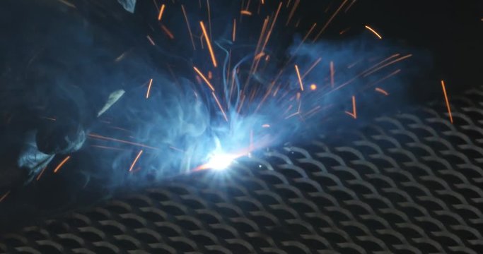 Close-up of welding torch and flame, then zoom out to man welding