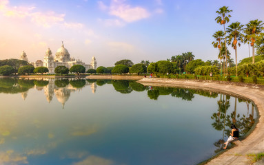 Victoria Memorial Kolkata at sunrise with a young female tourist sitting by the lake side.