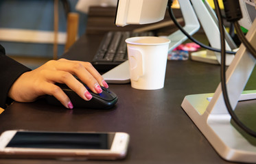 The young woman's hand is using a mouse to work The phone is placed on the desk in front of the computer.
