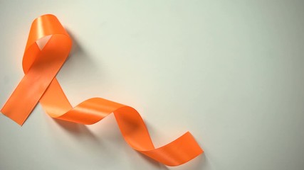Female placing orange ribbon on table, leukemia awareness campaign, precaution