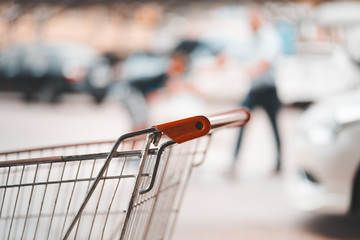 handle of shopping cart and blurred walking man with kid at parking lot, autumn color tone © angyim