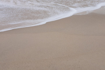 Fototapeta na wymiar Wave of the sea and white clean foam on the sandy beach