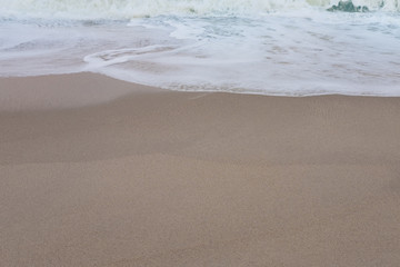 Wave of the sea and white clean foam on the sandy beach