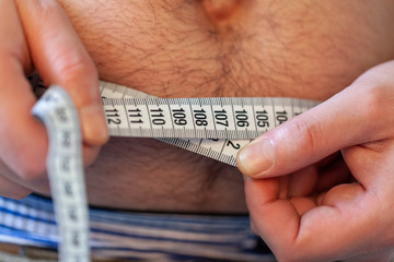 man measures her abdomen with a measuring tape