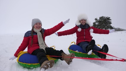 children slides in snow on an inflatable snow tube and waves hand. Happy girls slides through snow on sled. kids playing in park for Christmas holidays in winter