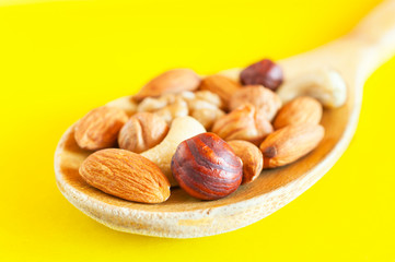 Almonds, Hazelnuts, Walnuts, Cashew Nuts in a Wooden Spoon Isolated on Yellow Background. Healthy Organic Snack, Breakfast, Food Ingredients.