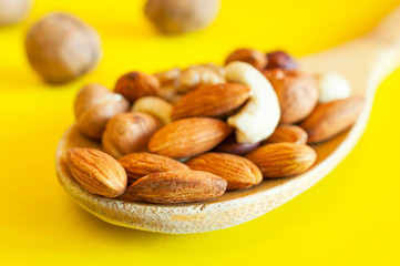 Almonds, Hazelnuts, Walnuts, Cashew Nuts in a Wooden Spoon, and Three Whole Walnuts Isolated on Yellow Background. Healthy Organic Snack, Breakfast, Food Ingredients.