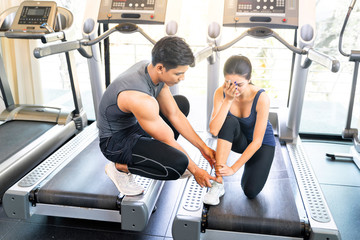 Fototapeta premium fitness coach is checking his student who sprained her ankle when running on the treadmill in the gym