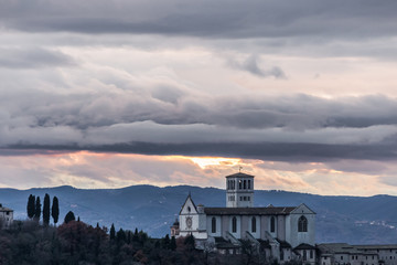 Beautiful view of St.Francis church in Assisi town (Umbria, Italy) from an unusual place at sunset, with moody clouds in the sky