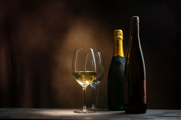 Two bottles with two glasses of wine on a wooden table in the dark of the night.