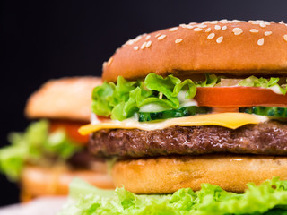 Fresh yummy grilled burgers on black background. Meat patty, tomatoes, cucumber, lettuce and sesame seeds. Fast food concept. junk food lifestyle