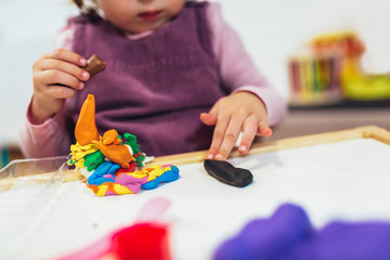 Naklejka premium Kid girl is playing with plasticine while sitting at table in nursery room.