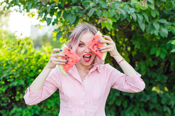 Fototapeta premium Beautiful young woman with pink hair holding two slices of watermelon in front of her face