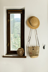 wicker hat and bag hang on a white wall in the hallway at home