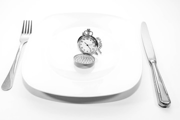 Monochrome image, old pocket watch on white plate, cutlery, conceptual image of needing more time.