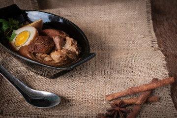stewed eggs and pork in black bowl and spices, spoon stainless steel place in front of on Sack and wood background
