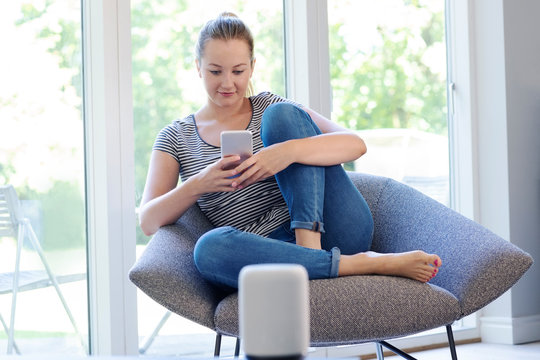 Woman At Home Streaming Music From Mobile Phone To Wireless Speaker