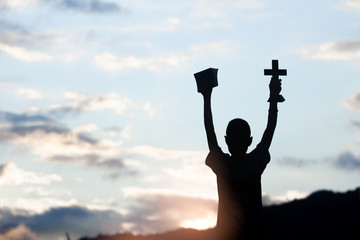 Boy holding christian cross and bible with light sunset background,christian concept.