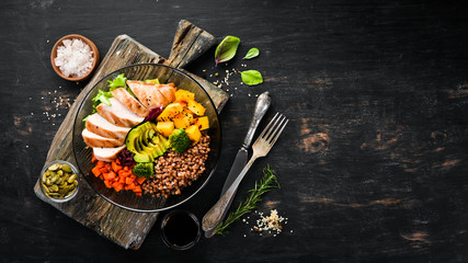 Bowl Buddha. Buckwheat, pumpkin, chicken fillet, avocado, carrots. On a black background. Top view. Free space for your text.