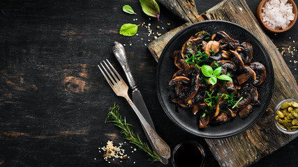 Fried mushrooms with parsley on the plate. On a black background. Top view. Free space for your text.