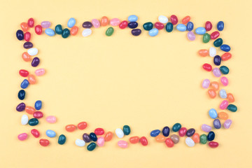 Jelly bean sweets in a rectangular bowls on yellow background frame in flat lay