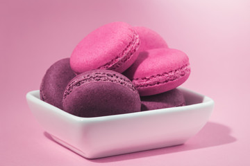Several sweet tasty pink macaroons in white bowl on pink background with copy space closeup