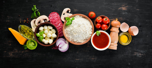 Ingredients for pizza. Mushrooms, sausages, tomatoes, vegetables. Top view. On a black wooden background. Free copy space.